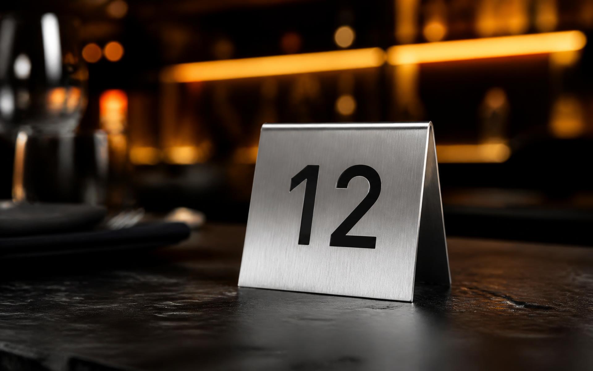 Número de mesa en acero inoxidable grabado, sobre mesa de restaurante con iluminación cálida